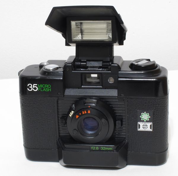 Hanimex 35 Micro-Flash
Période de production : 1980 à ? - Japon - n° 1 036 462
Type : compact
Format : 24x36 mm sur film 135
Viseur : clair collimaté
Objectif : 1:2.8 f=32 mm - mise au point par icônes
Mesure de l'exposition : posemètre sélénium
Sensibilité du film : 60-400 ASA
Obturateur : central 1/60 s et 1/125 s
Déclencheur : sur le capot
Synchronisation : flash intégré NG 10
Griffe : non
Ecrou de pied : oui
Armement et avance du film : molette canelée - compteur de vues avec remise à zéro automatique
Rembobinage du film : bouton et manivelle télescopique sur le capot
Ouverture du dos : par traction sur le bouton de rembobinage
Alimentation : 2 piles AAA de 1,5 v
Dimensions : 101 x 70,5 x 42 mm
Poids : 190 g HANIMEX 35 MICRO FLASH OUVERT.jpg
