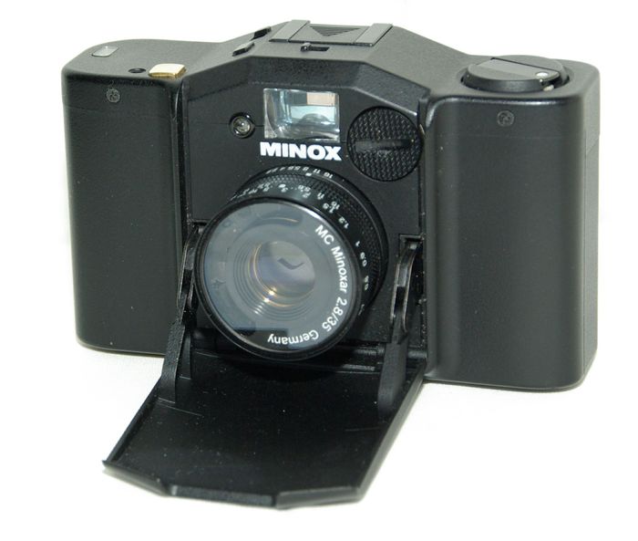 Minox Goldknopf
Période de production : 1991-1993 - Allemagne - n° 70656, série de 720 exemplaires
Type : compact à objectif fixe
Format : 24 x 36 mm sur film 135
Viseur : collimaté avec correction de la parallaxe
Objectif : MC Minoxar 1:2.8 f=35 mm avec filtre incorporé - mise au point de 0,7 m à l'infini
Mesure de l'exposition : automatique avec priorité à l'ouverture par cellule CDS couplée
rappel des vitesses dans le viseur avec zones de sous ou sur-exposition
Double exposition : oui, par interrupteur sur le capot
Sensibilité du film : 25 à 1 600 ASA
Obturateur : central électronique de 30 s à 1/500 s
Retardateur : 10 s, actionné par interrupteur sur le capot
Déclencheur : sur le capot (plaqué or 24 K d'où le nom Goldknopf en allemand) - filetage sur le capot pour déclencheur souple
Synchronisation : X à 1/125 s - contact central sur la griffe
Griffe : oui
Ecrou de pied : oui
Armement : levier à deux manoeuvres - compteur de vues avec remise à zéro lors de l'ouverture du dos
Rembobinage du film : par bouton et manivelle télescopique
Ouverture du dos : par verrou dans l'embase
Dos dateur : D-35G alimenté par 1 pile CR2025
Alimentation : 1 pile PX27 - bouton de test
Dimensions : 100 x 61 x 34 mm
Poids : 190 g
MINOX GOLDKNOPF OUVERT.jpg