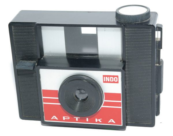 Aptika version 1
Période de production : 1968 à 1980
Type : Fixfocus en polystyrène à dos amovible
Variations : deuxième boîtier de l'Impera - 1 protubérance et 1 téton dans la chambre noire
synchronisation 2 broches - verrous plastiques - support bobine denté sans rivet
guides de bobine en plastique
Format : 4 x 4 cm sur film 127
Viseur : clair centré sur le capot
Objectif : ménisque - MAP de 1,5 à l'infini - diaphragme fixe
Mesure de l'exposition : sans
Obturateur : central à secteur à une seule vitesse et sans armement préalable
Déclencheur : sur l'obturateur
Synchronisation : deux broches
Griffe : sans
Ecrou de pied : sans
Avance du film : par bouton moleté, contrôle par une fenêtre rouge au dos,
sans protection contre les doubles expositions
Rembobinage du film : sur bobine réceptrice
Ouverture du dos : par 2 verrous
Chargement du film : sur le boîtier
Alimentation : sans
Transport : 2 oeilletons
Dimensions : 125 x 91 x 54 mm
Poids : 177 g Indo Aptika 82.jpg